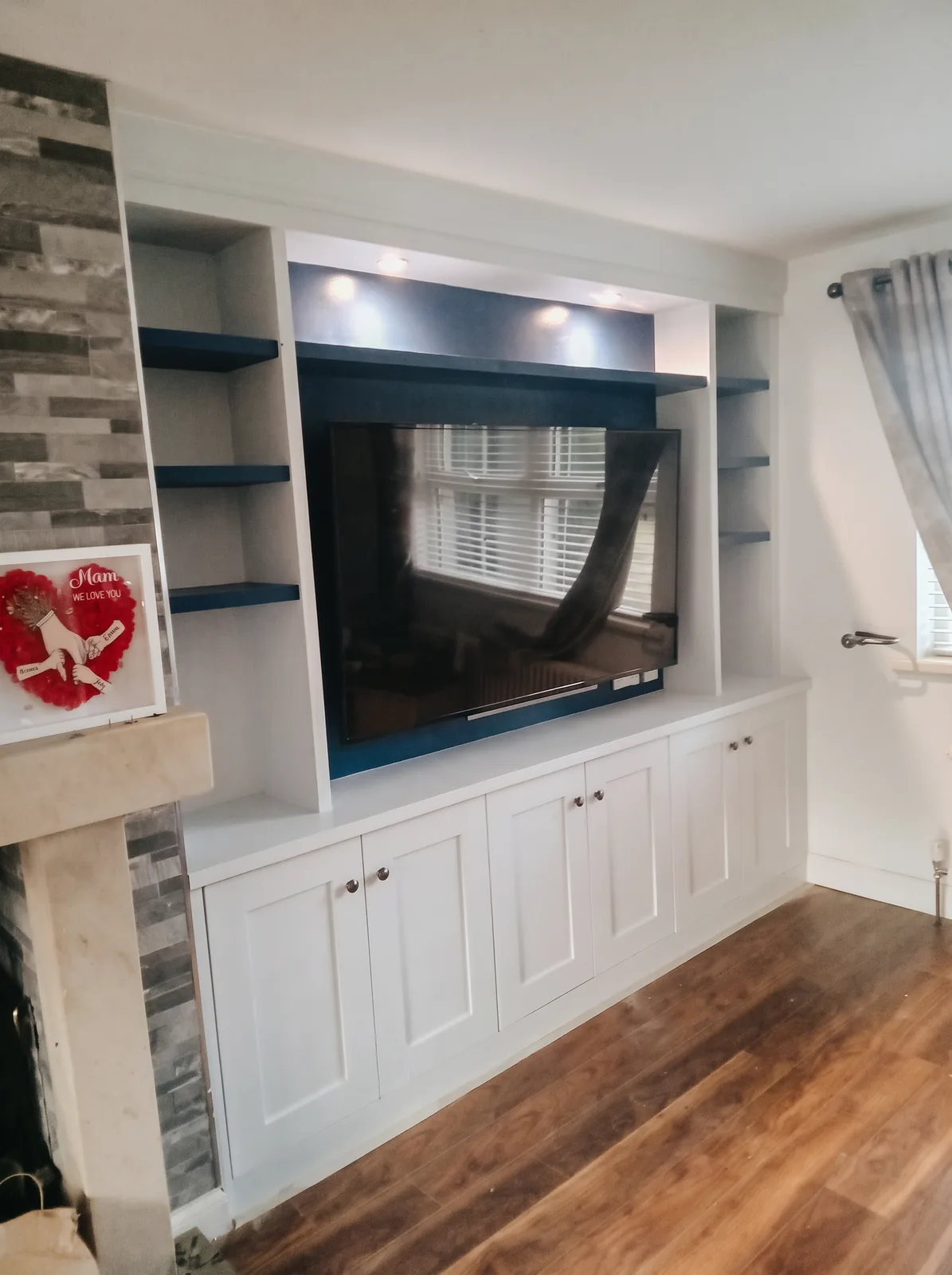 White fitted shelving and cupboards with a navy-backed TV recess and navy floating shelves