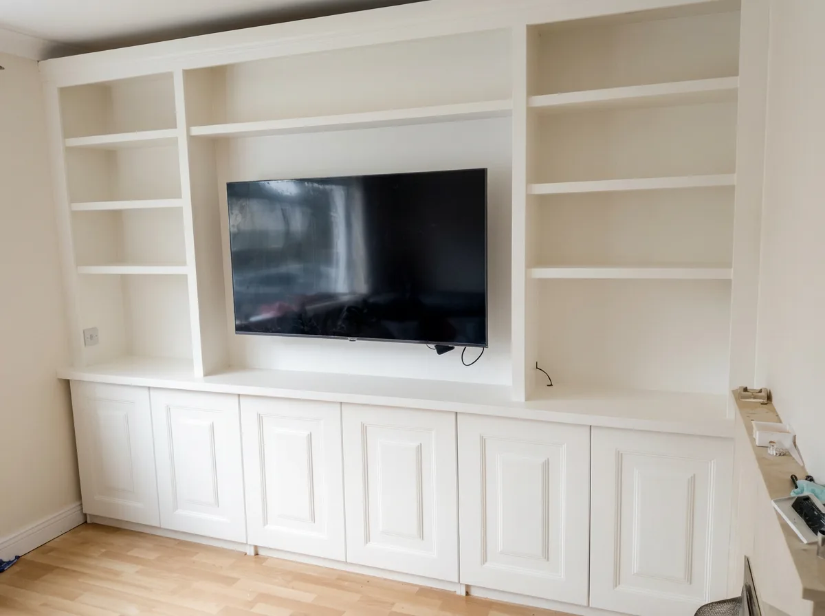White fitted wall of open shelving around a TV, above a long run of raised-panel cupboards