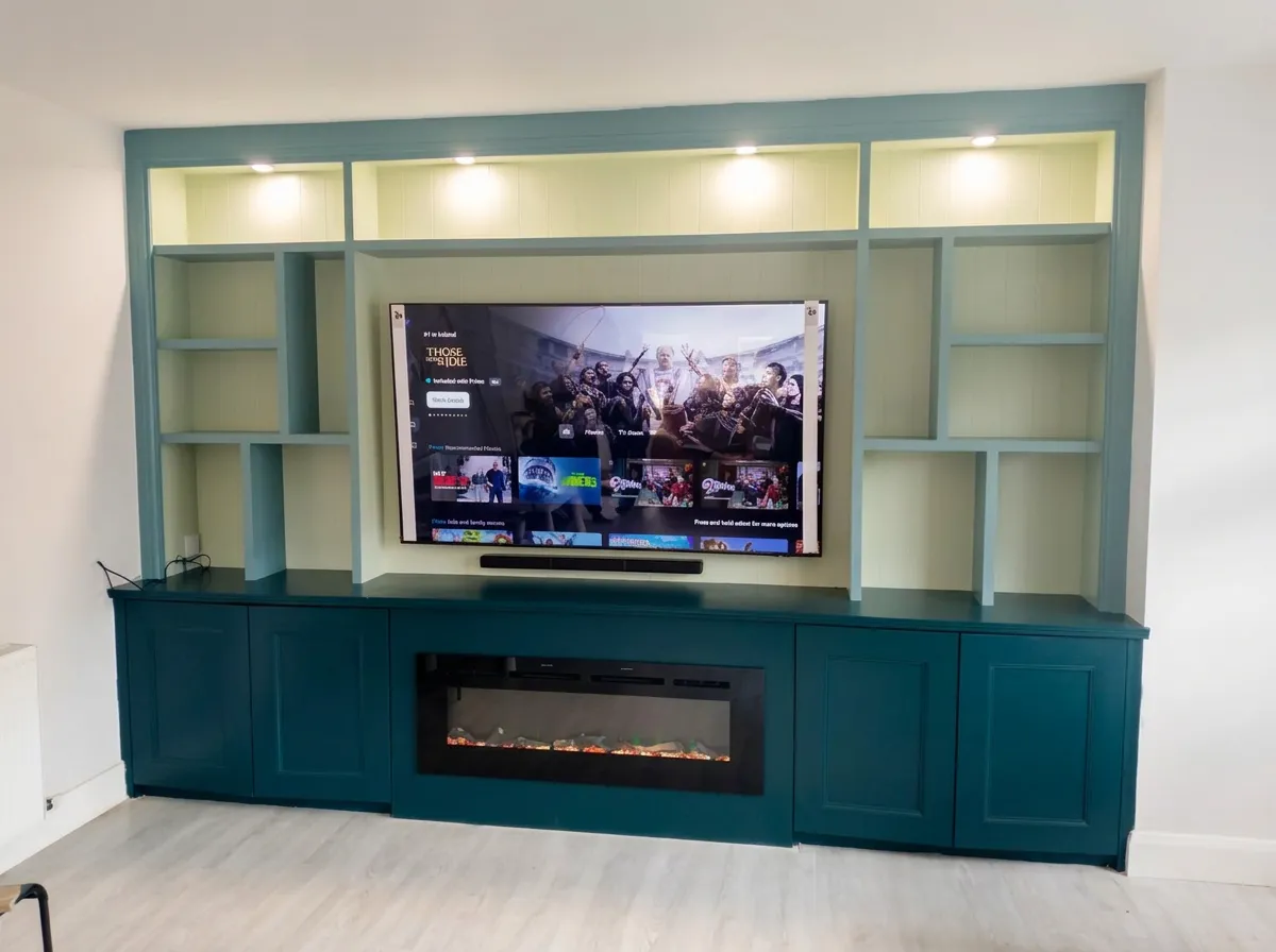 Teal fitted media wall with lit open shelving, panelled cupboards and a long inset fire