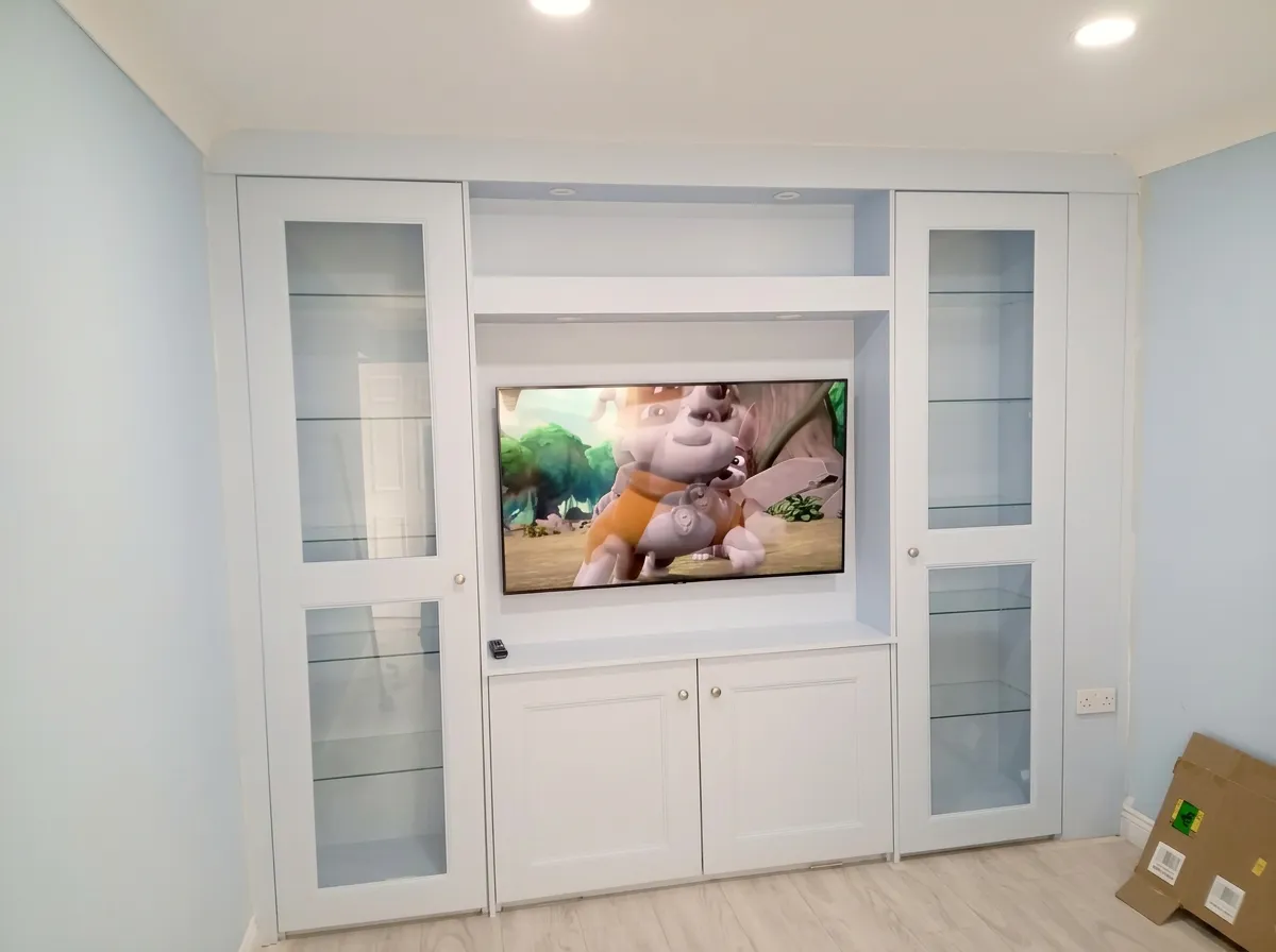 White fitted media wall with glazed display cabinets either side of the TV and panelled cupboards below