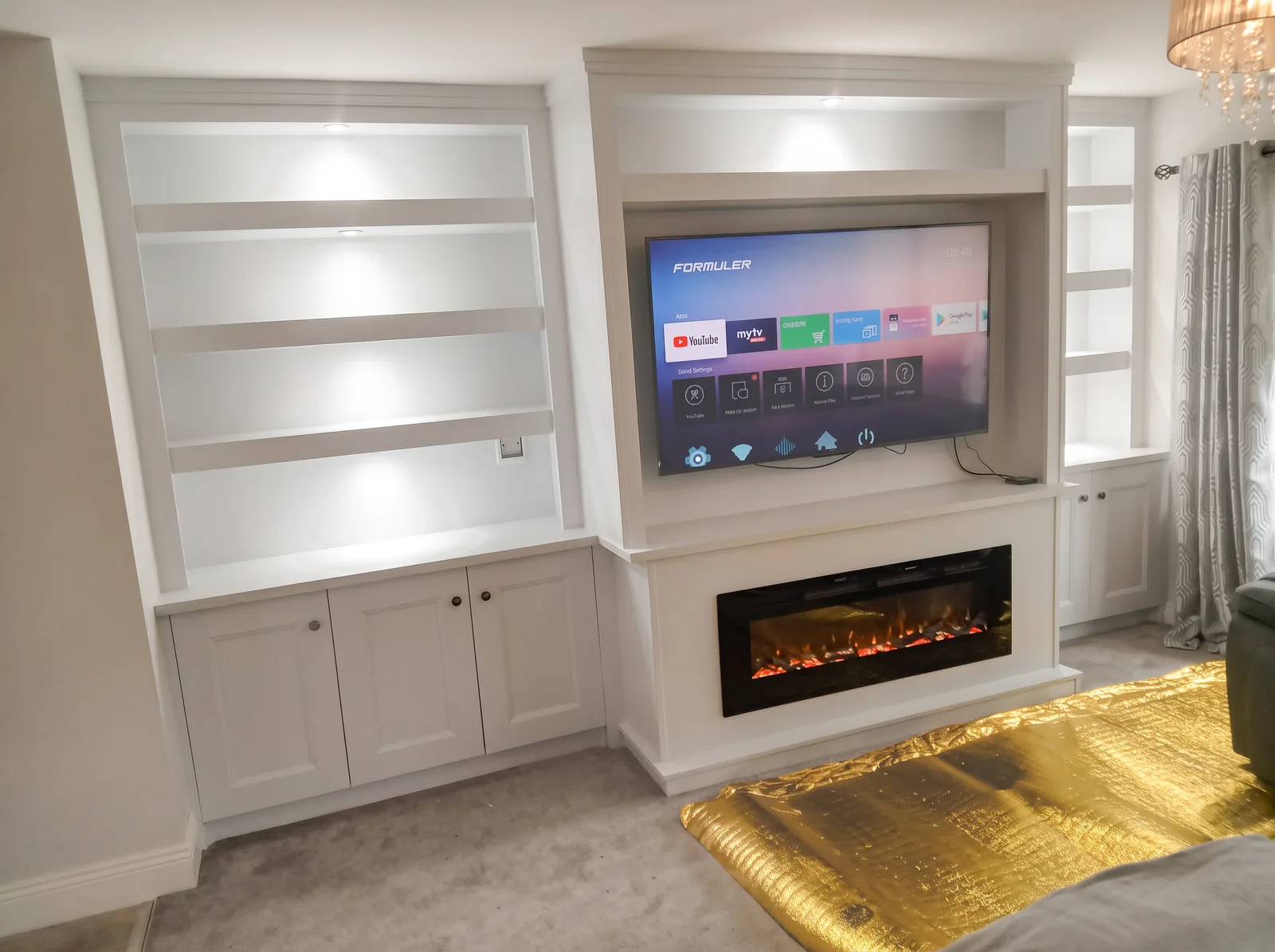 White alcove shelving with downlights, Shaker cupboards and a raised fire surround beneath the TV