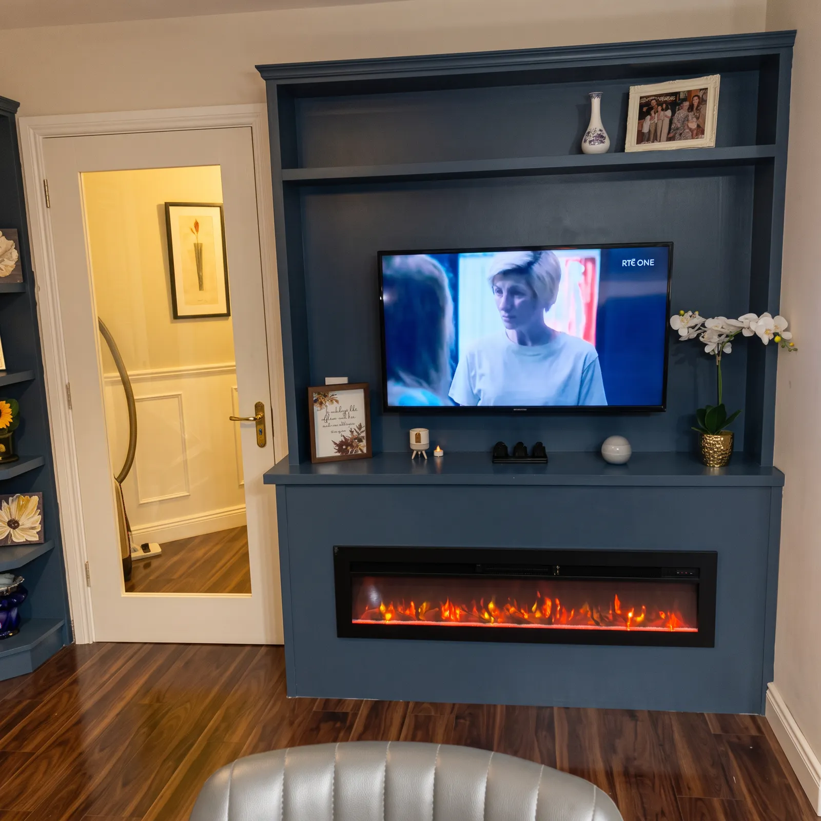Deep navy fitted media wall with open shelving, wall-mounted TV and a wide inset electric fire