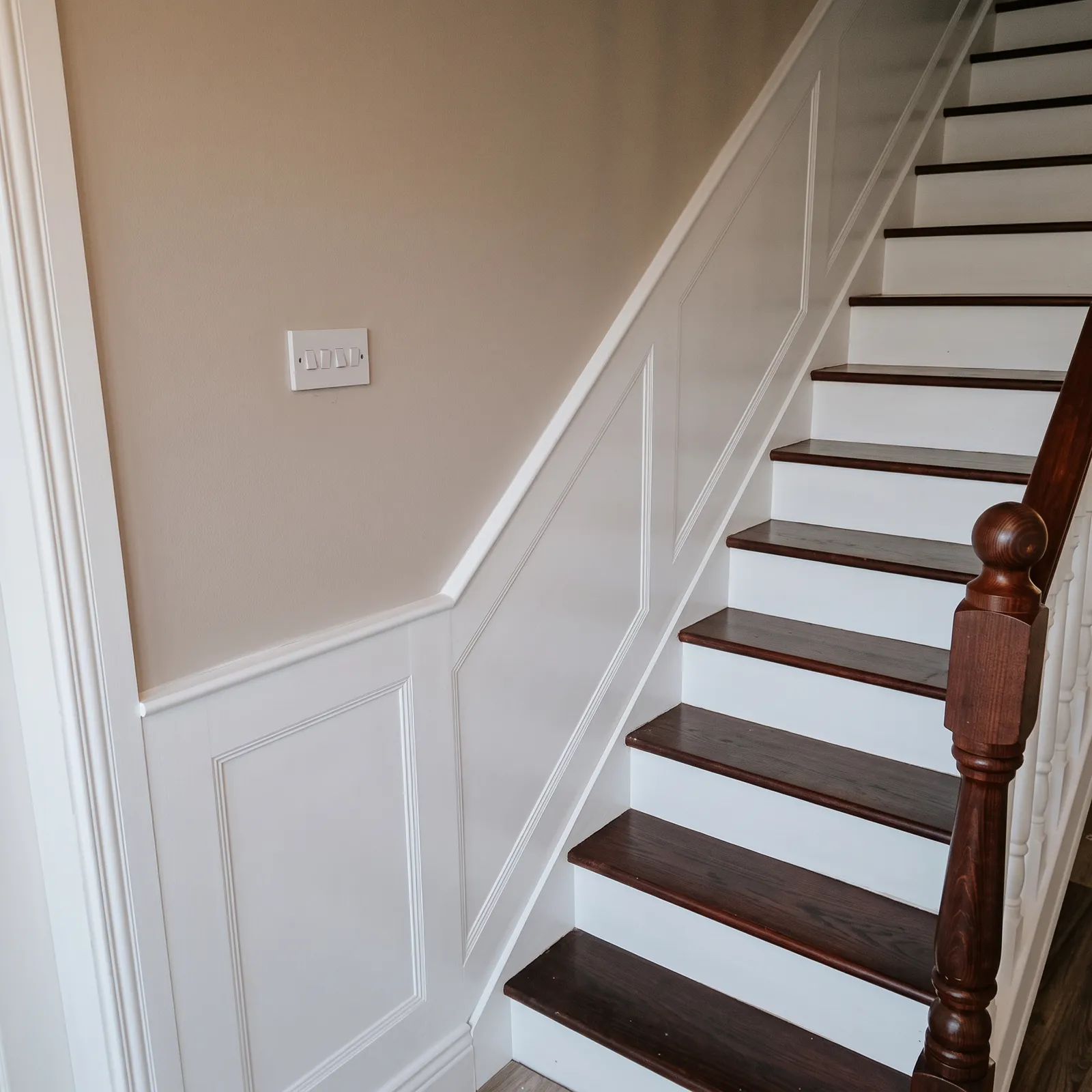 Stairway wall finished in white panel moulding alongside dark-stained stair treads